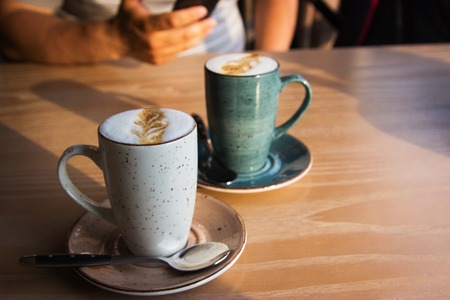 Latte on wooden table in cafe man hands with telephone. Selective focus. Horizontal.の写真素材