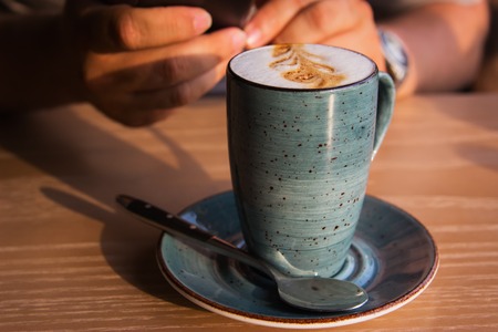 Latte on wooden table in cafe man hands with telephone Selective focus Horizontal.