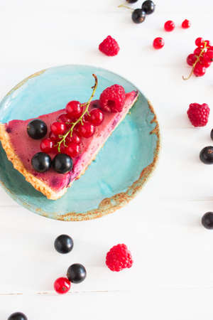 Wedge appetizing scattered mix raspberry currant tart top view blue plate.