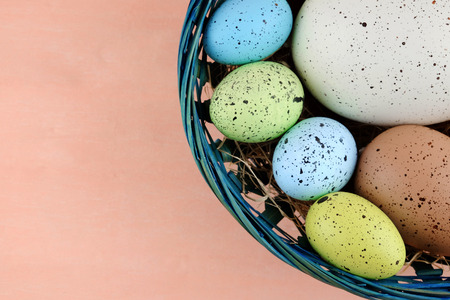 Easter colorful quail eggs of different sizes in the blue basket on a pale pink background.