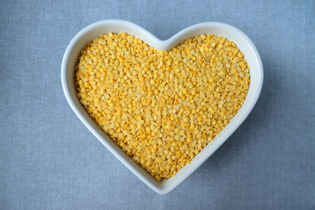 Yellow lentils in a bowl in the shape of heart  on the blue-grey background.の写真素材