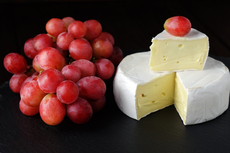 Cheese brie and fresh red grapes on slate tile and dark background.