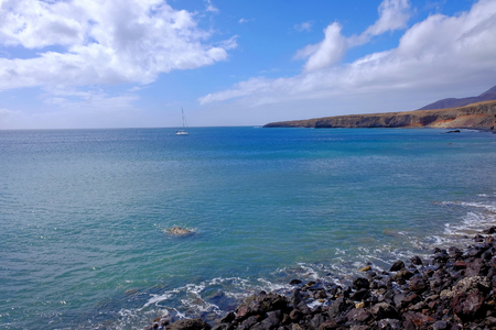 View on the beach Las Coloradas with blue ocean water and a white sailboat. Location Morro Jable, Fuerteventura, Canary Islands, Spain.の写真素材