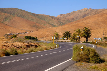 Typical landscape with curved road in red volcanic mountains and a small village close to betancuria on the Canary Island Fuerteventura, Spain.の写真素材