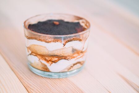 Italian dessert tiramisu in a transparent glass on a wooden table.