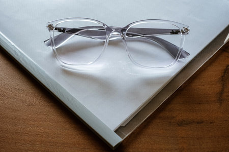 Glasses in a transparent frame on a map with white paper on wooden table, close-up.