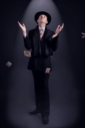 business man in a top hat to catch money flying out of the light beamの写真素材