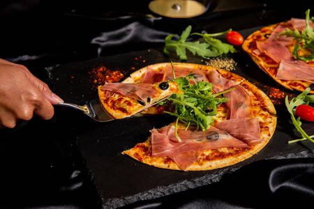 Pizza Jamon IbÃ©rico and Rocket salad served on slate table, black background, top viewの写真素材