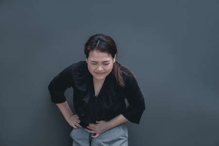 Young asian woman suffering from stomach painful illness feeling unwell. Isolate on dark backgroundの写真素材