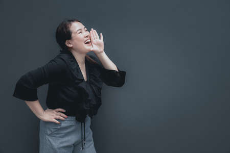 Excited young asian woman shouting with hands cupped around mouth isolated on grey background with copy spaceの写真素材