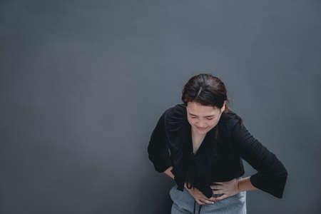 Young asian woman suffering from stomach painful illness feeling unwell. Isolate on dark backgroundの写真素材