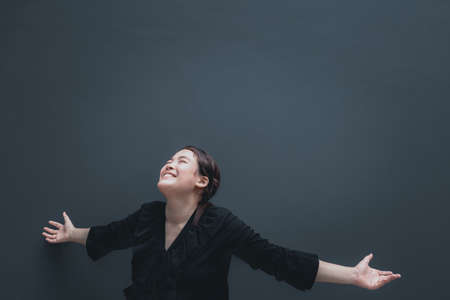 Happy excited young asian woman open her arms to the sky and enjoying life celebrating and success. Isolated on dark background with copy spaceの写真素材