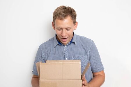 curious man looking inside a cardboard box he holds in his hands on a white background