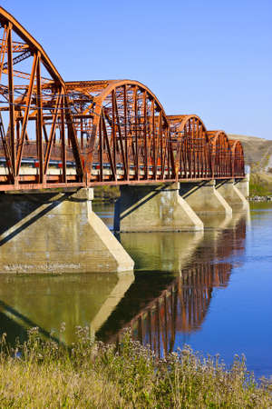 Old red bridge over the calm waters of the Saskatchewan River near Outlook on the Canadian Prairies.の写真素材