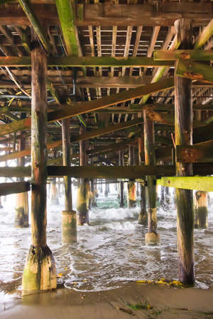 Waves crashing underneath a pier while the tide is rolling out.の写真素材