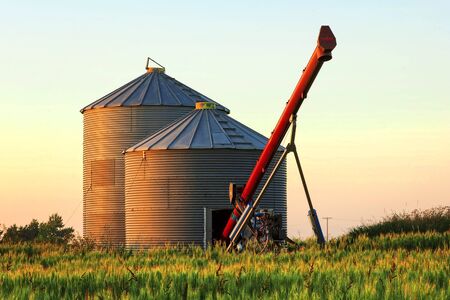 Pair of grain bins and an auger in the middle of a fieldの写真素材