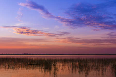 Red and orange glow of the sun over the calm waters of the lake at sunsetの写真素材