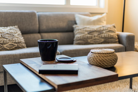 A coffee table with a book and a mug on it. The table is in a living room with a couch and a window. Scene is cozy and relaxingの写真素材