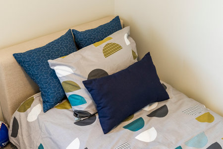 A bed with a gray and blue comforter and pillows. The pillows are blue and green and the comforter...