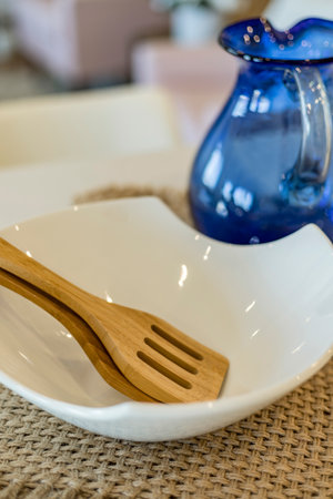A blue pitcher sits next to a white bowl and wooden spatula. The bowl is empty and the pitcher is...