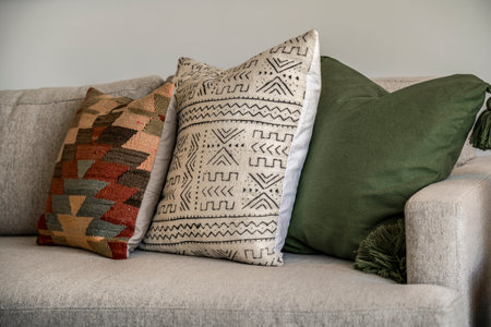 Three pillows are on a couch, with one being green and the other two being multicolored. The green pillow has a pattern of lines and dots, while the other two have a more abstract designの写真素材