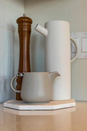 A white pitcher and a wooden pepper grinder are on a marble countertop. The pitcher is filled with water and the grinder is empty. The scene is simple and cleanの写真素材