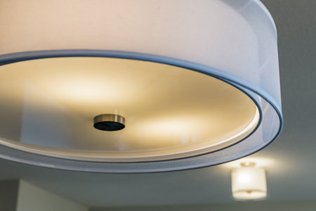 A white light fixture with a silver base. The light is on and the bulb is glowing. The light fixture...