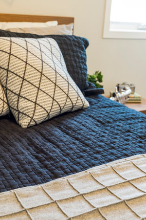 A bed with a blue comforter and a white pillow. The bed is made and the pillows are neatly arranged