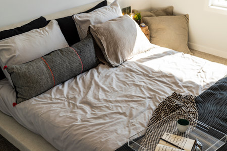 A bed with a white comforter and black and white pillows. A tray with a cup and a book is on the bed