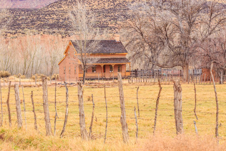A rustic farmhouse sits in a field with a fence around it. The house is surrounded by a fence and a few trees. The scene is peaceful and serene, with the houseの写真素材