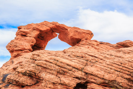 A large rock formation with a small hole in the middle. The rock is red and the sky is blueの写真素材