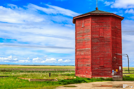 A red building with a pointed roof sits in a field. The building is surrounded by grass and he is abandoned. The sky is clear and blue, and there are no clouds in the skyの写真素材