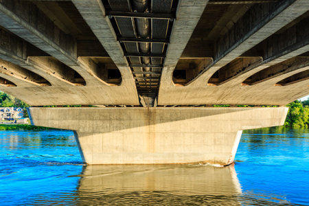 A bridge is shown from the underside, with the water below and the sky above. The bridge is made of...