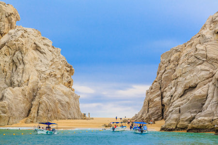 A group of people are on boats in the ocean near a rocky shore. The sky is clear and the water is...