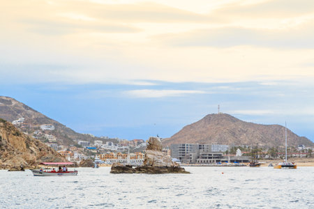 A boat is floating in the ocean near a rocky shore. The sky is cloudy and the water is calmの写真素材