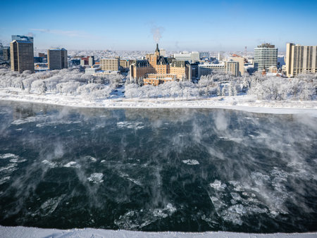 A city with a large building in the background and a river in the foreground. The city is covered in snow and the river is frozenの写真素材