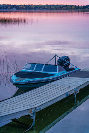A small boat is sitting on a dock by a lake. The water is calm and the sky is a beautiful shade of pinkの写真素材