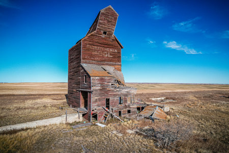 A large, old, abandoned building with a slanted roof. The building is surrounded by a dry, barren landscapeの写真素材