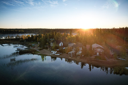 A beautiful lake with a sunset in the background. The sun is setting and the sky is a mix of orange and pink. The lake is surrounded by trees and housesの写真素材