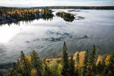 A beautiful lake with trees in the background. The water is calm and the sky is clear. The trees are...