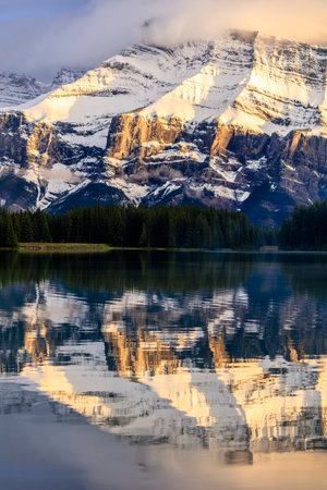 A mountain range is reflected in the water of a lake. The mountains are covered in snow and the water is calmの写真素材