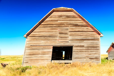 A large, old barn with a window in the middle of the wall. The barn is empty and the sky is blue