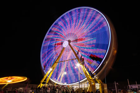 A colorful merry go round with people on it. The lights are on and the people are enjoying themselvesの写真素材