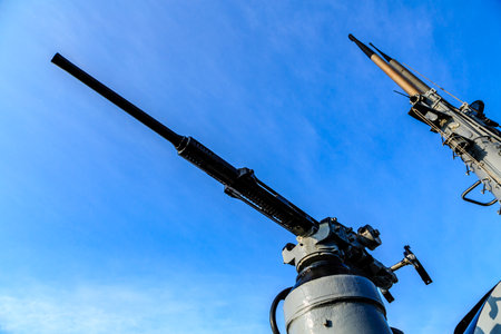 A gun is pointed up at the sky. The sky is blue and clear. The gun is old and rustedの写真素材