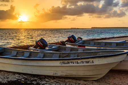 Three small boats are sitting on the beach, one of which is labeled Yellow Sea. The sun is setting in the background, casting a warm glow over the sceneの写真素材