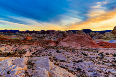 A beautiful sunset over a rocky desert landscape. The sky is filled with clouds and the sun is setting, casting a warm glow over the rocks. The scene is serene and peacefulの写真素材