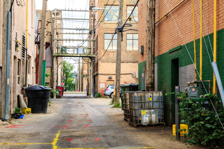 A narrow alleyway with a few trash cans and a few cars parked on the side. Scene is somewhat bleak and uninvitingの写真素材