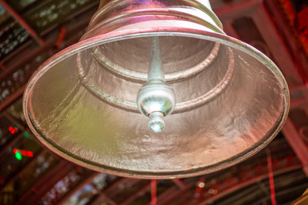 A large bell hanging from the ceiling. The bell is silver and has a gold top