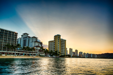 A beautiful sunset over a beach with a city skyline in the background. The water is calm and the sky is a mix of orange and pink huesの写真素材