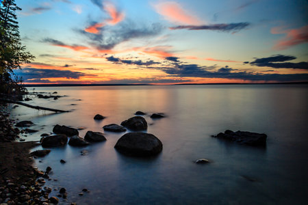 A beautiful sunset over a lake with a rocky shoreline. The sky is filled with clouds and the water is calmの写真素材